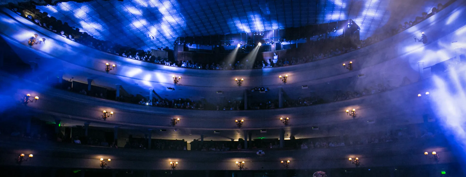 Foto panoramica del escenario hacia las butacas, lleno de personas viendo un evento